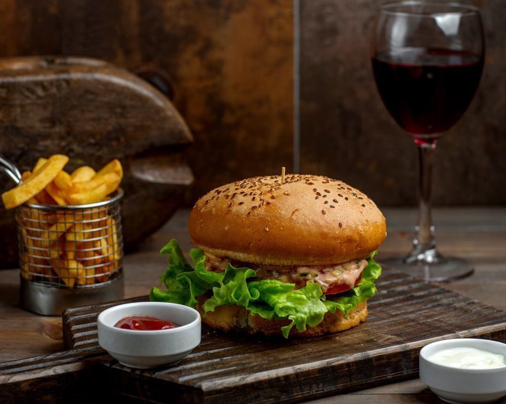 Burger gourmet servi avec frites croustillantes, sauces et verre de vin rouge sur table en bois